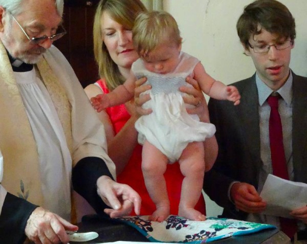 A hot smocked baby thinking he may as well jump into the font if he's going to have more water poured all over him